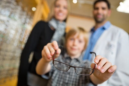Boy Showing Glasses With Mother And Optician In Store