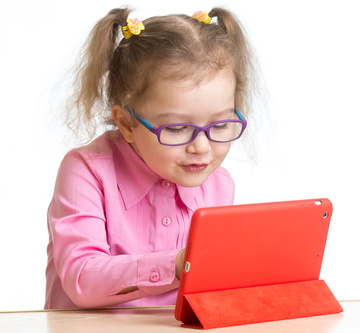kid in glasses looking at mini tablet pc screen sitting at table